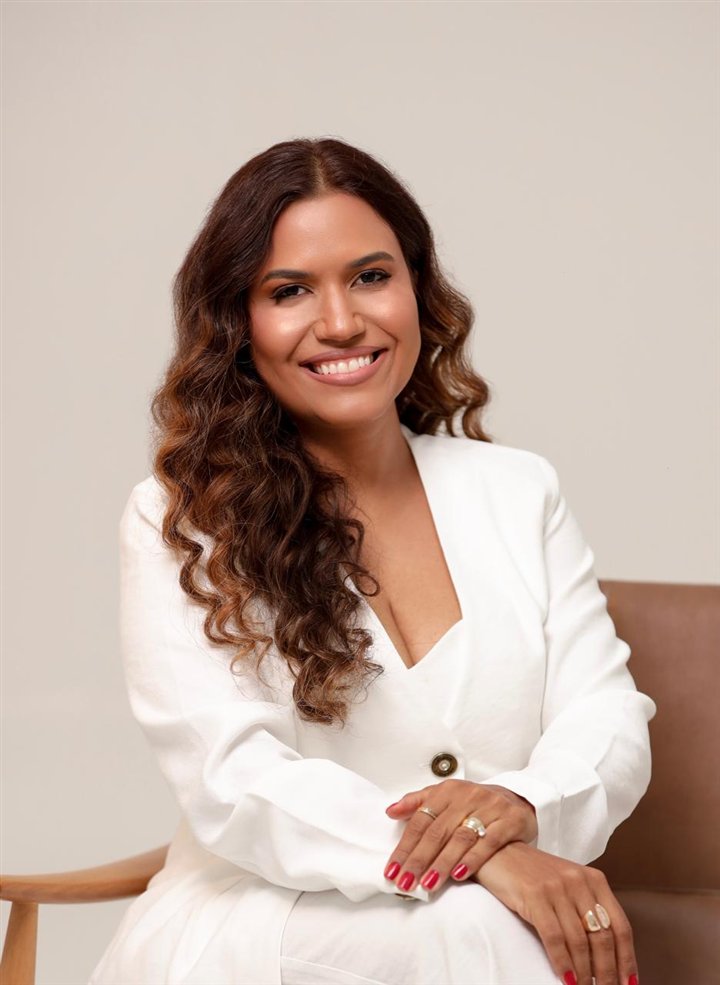 Jakelline Pimentel, advogada, de terno branco, sentada e sorrindo