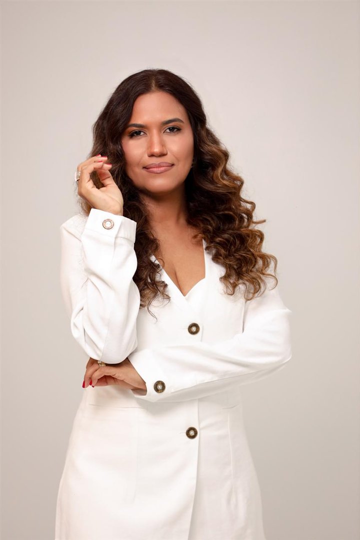 Jakelline Pimentel, advogada, de terno branco, em pé, com a mão junto ao cabelo